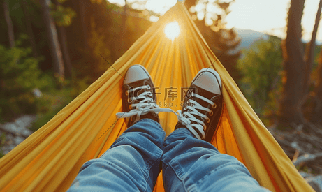 在温暖的夏日露营生活中穿着运动鞋和牛仔裤的男性腿躺在吊床上