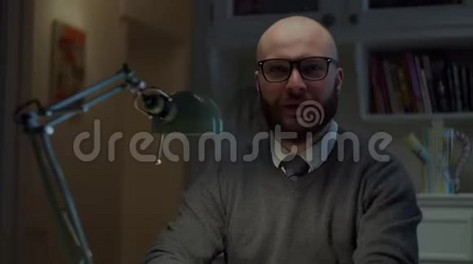 一个30多岁的大胡子戴眼镜的男人，用拇指向上看着家里的摄像机，有感情地说话。 在线教育过程。 网络摄像头