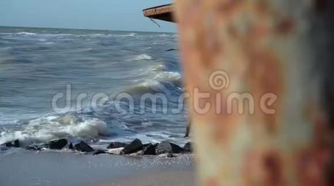 摄像机从海滩上一个行走的女孩身后一根生锈的金属杆上抽出