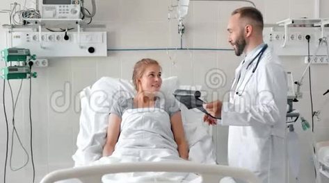 男医生在病床上与女病人交谈。 带剪贴板和x光照片的微笑医生