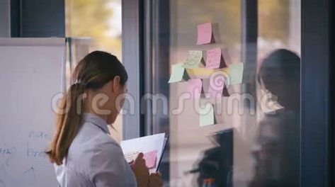 商务女性使用粘性笔记头脑风暴解决问题策略玻璃白板显示解决方案