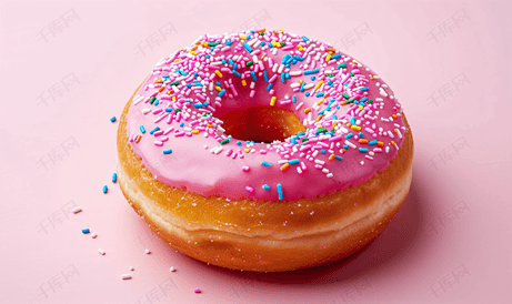 粉红色背景上撒着粉红色糖霜和彩色糖的甜甜圈