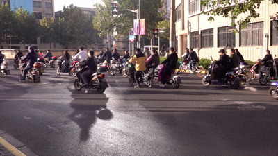 一群摩托车小摩托车和自行车在绿灯下冲过街道这是中国上海典型的