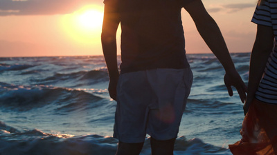 夕阳西下波涛汹涌的海边一对恩爱的情侣牵着手