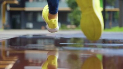 女运动员在户外慢跑踏入水坑一个跑步者在雨中奔跑造成飞溅慢动作