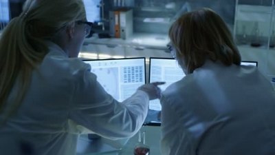 帆布鞋女的实拍视频素材资深女科学家与她的实验室助手讨论科学数据他们正在看两个显示在