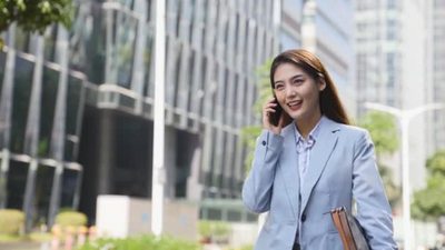 年轻的亚洲女商人走在现代城市的街道上打电话