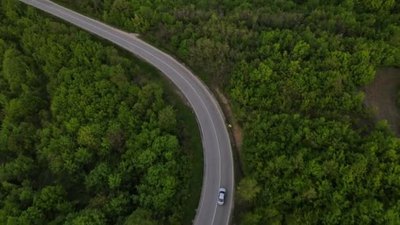 旅游实拍视频素材在塞尔维亚春车沿着蜿蜒的公路行驶时在山脉上一条弯曲的沥青路面