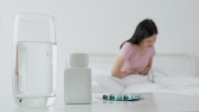 年轻的亚洲女人坐在床上痛胃