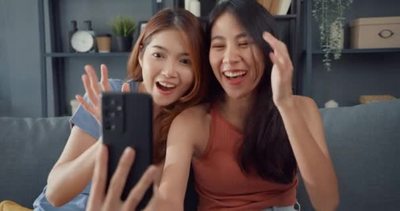 年轻的亚洲女人开心地笑着放松在家里客厅里使用智能手机视频通话