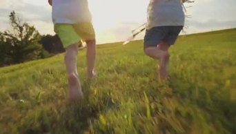 4K日出时分未知的女孩和男孩在绿茵的草地上奔跑