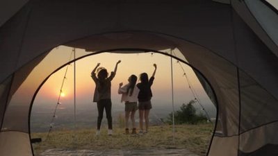 一群年轻的亚洲朋友站在帐篷前拍照和放松在夏营度假的傍晚夕阳西
