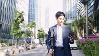 在现代城市，年轻的亚洲商人一边走在大街上一边看手机