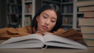 永远不回头实拍视频素材无聊悲伤疲惫懒惰的韩国年轻女子躺在大学图书馆的桌子上读无聊的